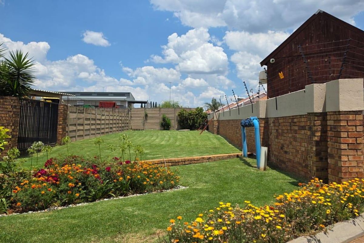 A well-maintained rear garden featuring a manicured lawn, established flower beds, and secure perimeter brick walling with electric fencing.