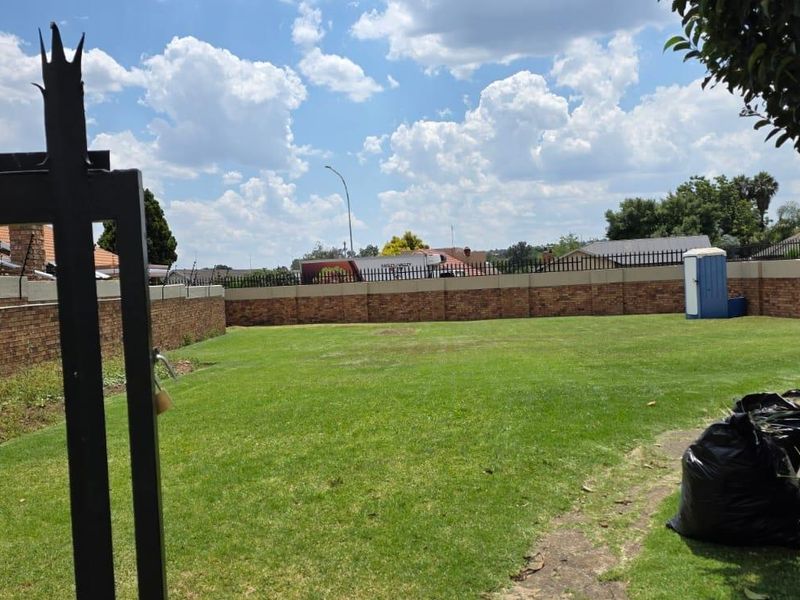 A spacious, enclosed private garden area featuring a brick perimeter wall, metal security fencing, and a well-maintained lawn.
