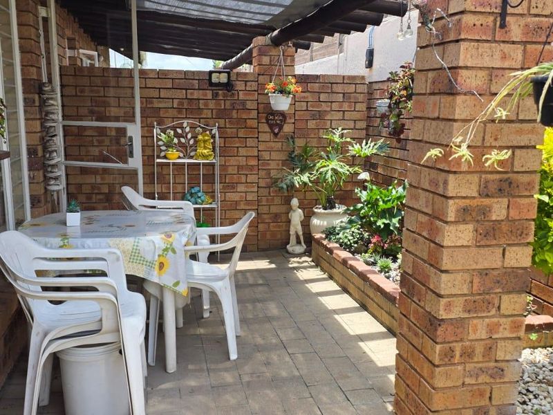 A covered patio area featuring exposed brick walls, paved flooring, and a built-in planter box, providing a cozy outdoor space.