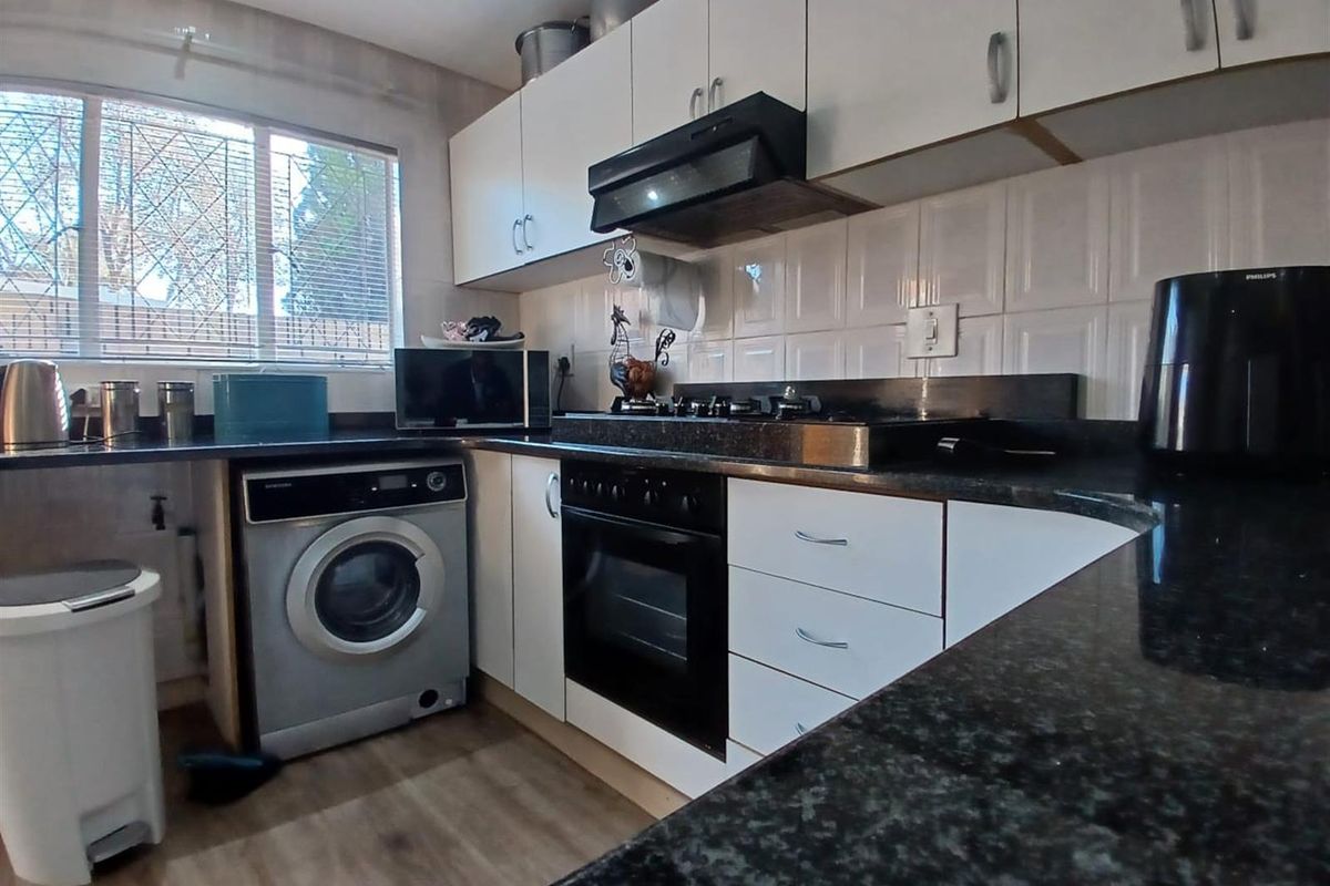 Functional kitchen featuring white cabinetry, dark granite countertops, built-in oven, gas hob, extractor fan, and integrated space for a washing machine.