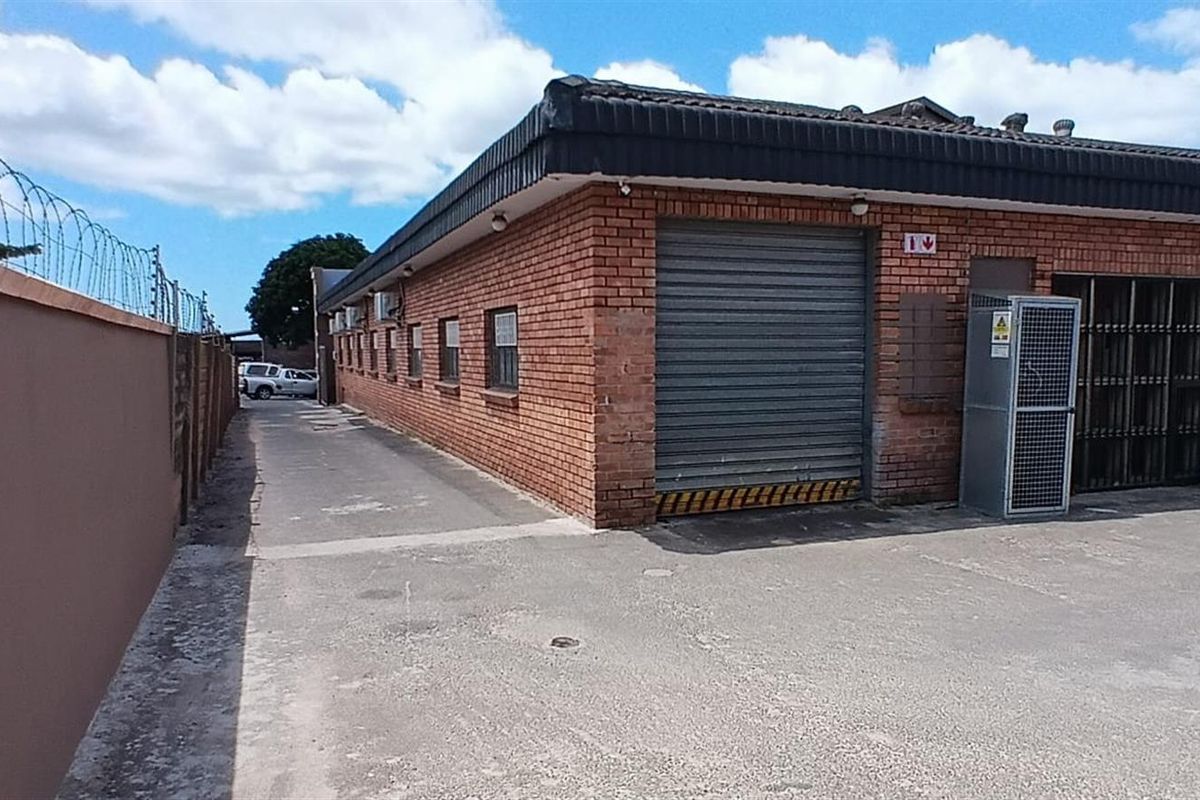 Commercial property exterior featuring a face brick facade, secure roller shutter access, and a paved driveway with perimeter security fencing.