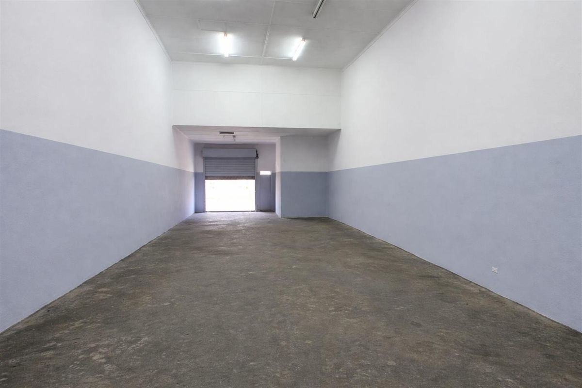 An empty commercial utility or storage space featuring concrete flooring, a roller shutter door, and functional overhead fluorescent lighting.