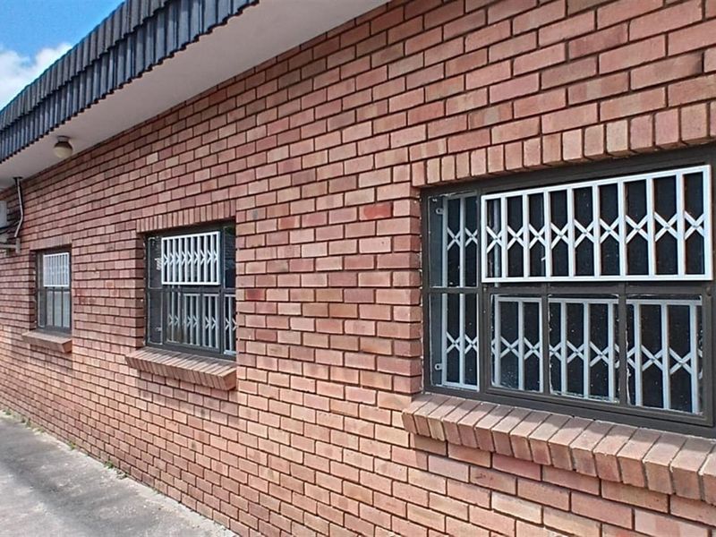 Exterior view of a commercial building featuring a face brick facade, security bars on windows, and wall-mounted air conditioning units.