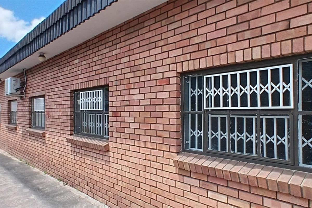 Exterior view of a commercial building featuring a face brick facade, security bars on windows, and wall-mounted air conditioning units.