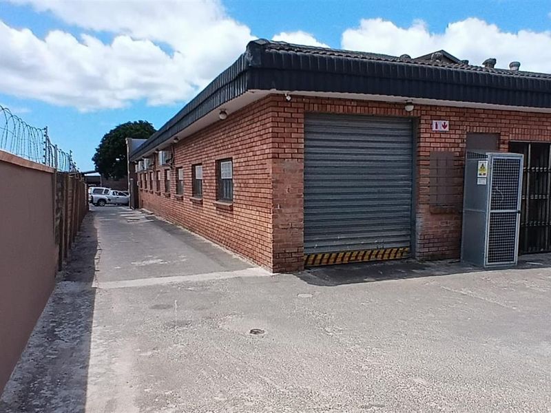 Exterior view of a commercial property featuring a brick facade, roller shutter access, and secure perimeter fencing with a concrete driveway.