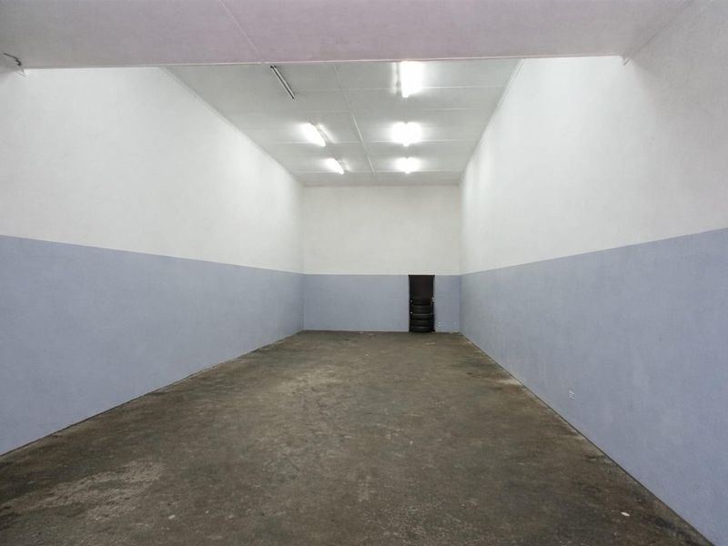 An empty, utilitarian commercial space featuring concrete flooring, dual-tone painted walls, and overhead fluorescent lighting, suitable for storage or workshop use.