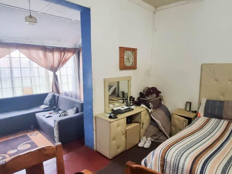 A bedroom featuring a large window and built-in vanity, showing signs of wear on the flooring and ceiling finishes.