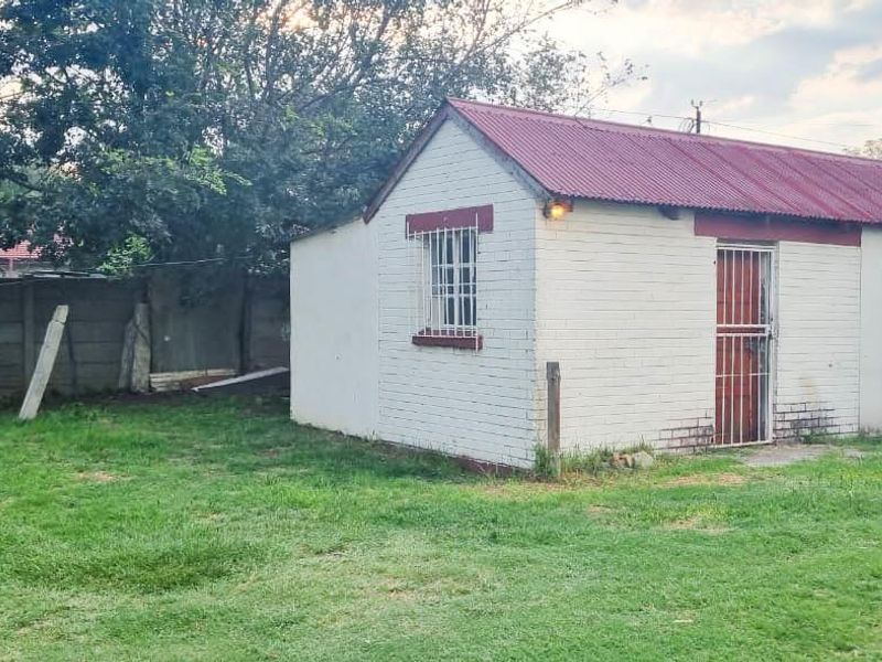 A detached outbuilding with a corrugated metal roof and security features, situated in a spacious backyard with precast concrete perimeter fencing.
