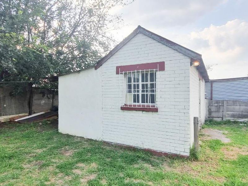 A view of the rear exterior of the property featuring a small brick structure with security bars and a surrounding precast concrete boundary wall.