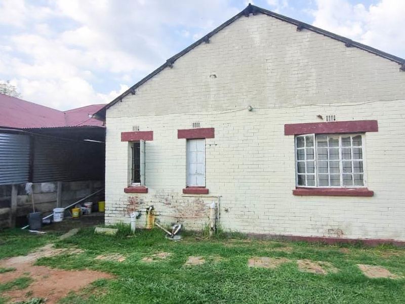 Rear view of the property showing a brick exterior, steel-framed windows, and a corrugated metal lean-to structure with visible maintenance requirements.