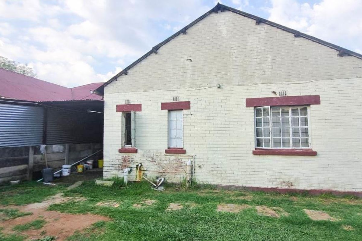 Rear view of the property showing a brick exterior, steel-framed windows, and a corrugated metal lean-to structure with visible maintenance requirements.