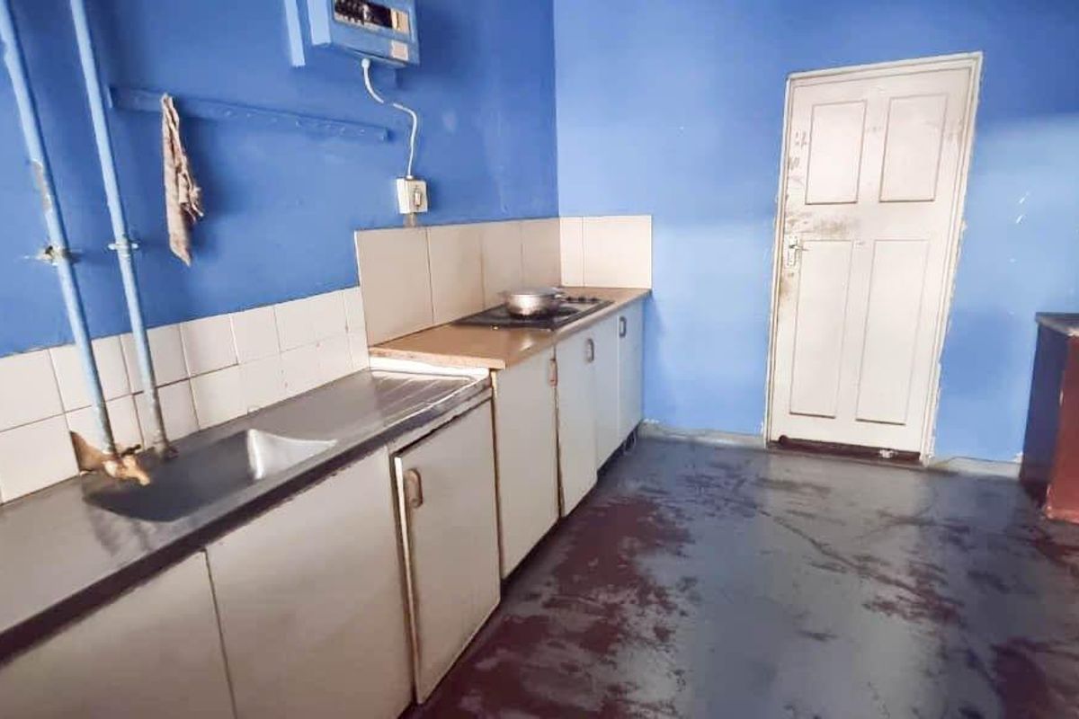 A basic kitchen area featuring built-in cabinetry, a stainless steel sink, and a hob, requiring cosmetic updates and flooring repairs.