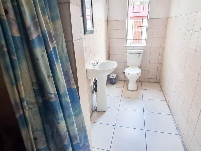 A functional bathroom featuring a pedestal basin, toilet, and tiled finishes throughout, offering a basic layout ready for modernization.