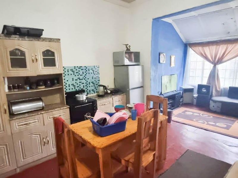 Open-plan living and kitchen area featuring built-in cabinetry, tiled backsplash, and large windows, offering a functional layout with potential for modern updates.