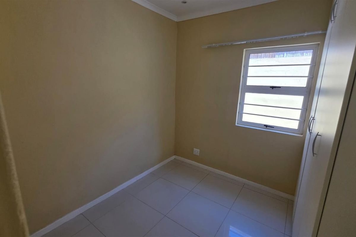 A compact, empty bedroom featuring neutral wall paint, tiled flooring, and a built-in wardrobe.