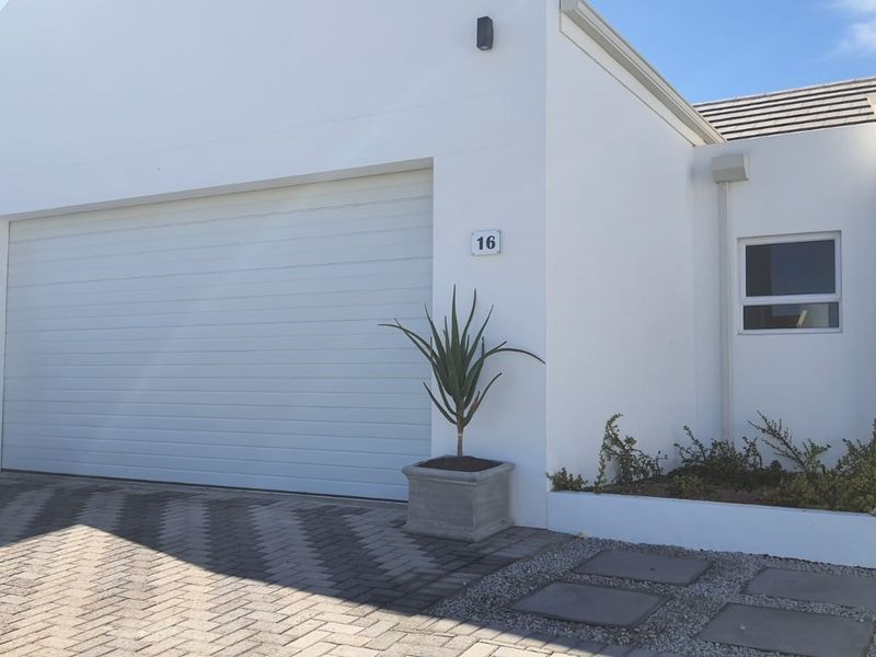 Front elevation of the property featuring a clean white facade, automated garage door, paved driveway, and a small landscaped garden bed.