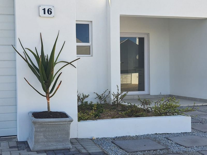 Modern front facade featuring a clean white finish, paved driveway, covered entrance, and a neat raised garden bed.