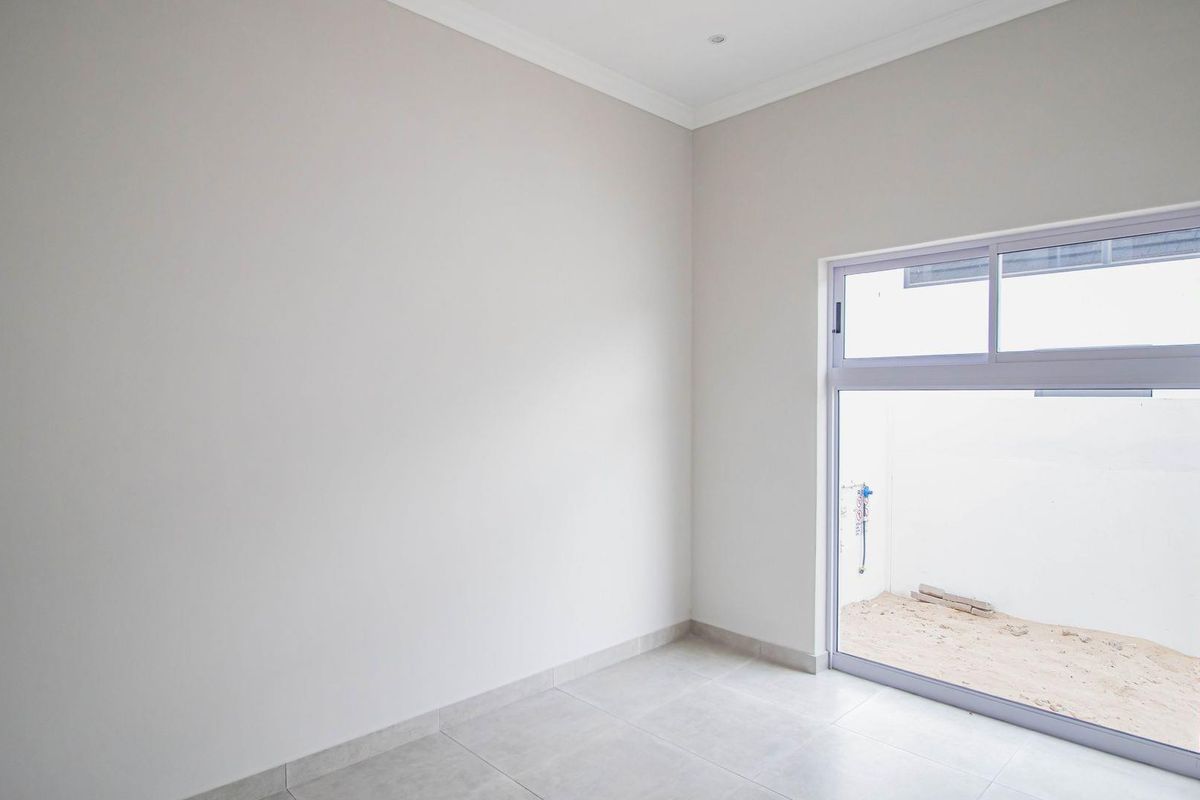 A bright, empty room featuring neutral wall finishes, tiled flooring, and a large sliding glass door providing access to an outdoor area.