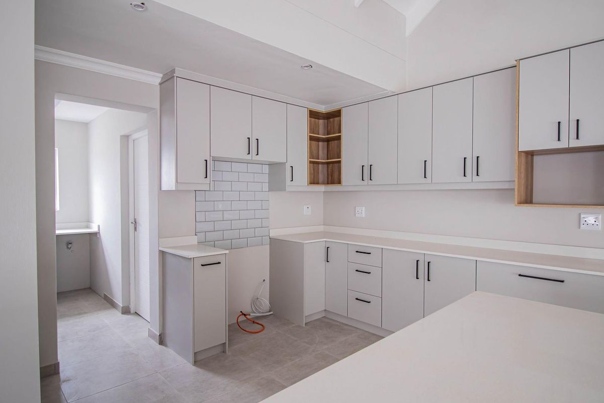 Modern kitchen featuring light grey cabinetry, stone countertops, subway tile backsplash, and an adjacent scullery area with neutral floor tiling.