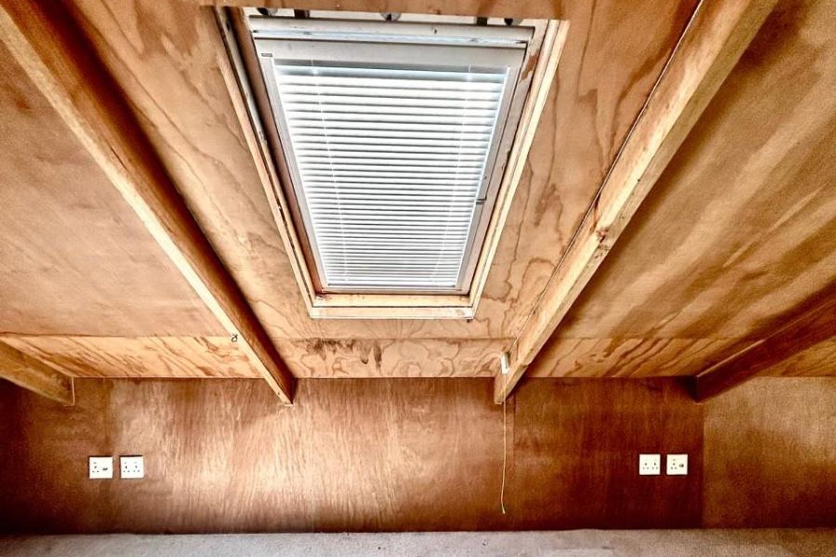 An attic-style bedroom featuring plywood paneling, a skylight window, and fitted electrical outlets, offering a rustic and functional living space.