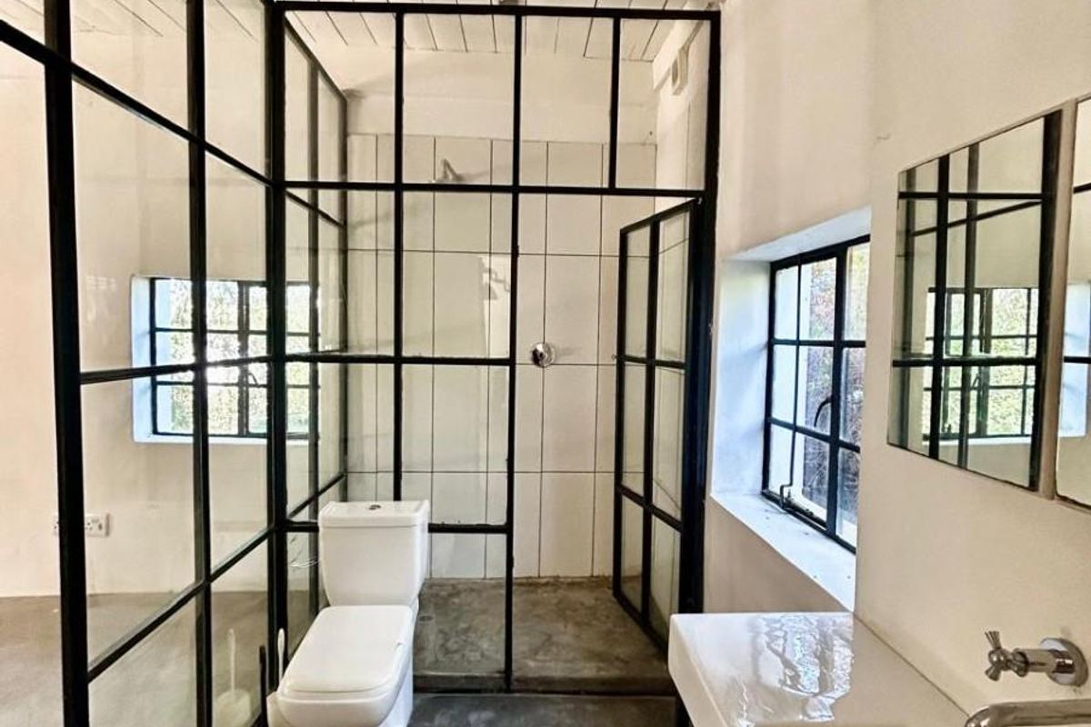 Modern industrial-style bathroom featuring a black steel-framed glass shower enclosure, white ceramic toilet, wall-mounted basin, and exposed timber ceiling beams.