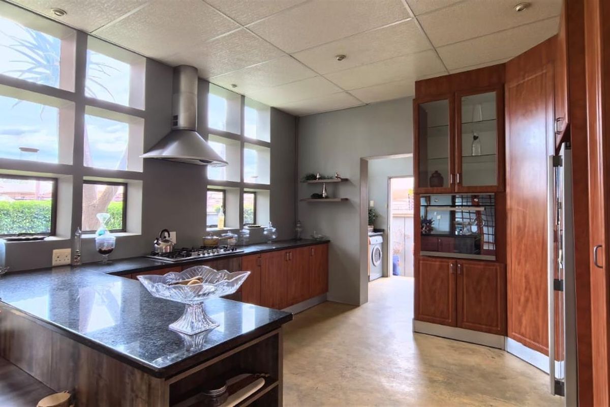 Spacious kitchen featuring dark wood cabinetry, granite countertops, a gas hob with extractor, and integrated oven, with a seamless flow to the laundry area.