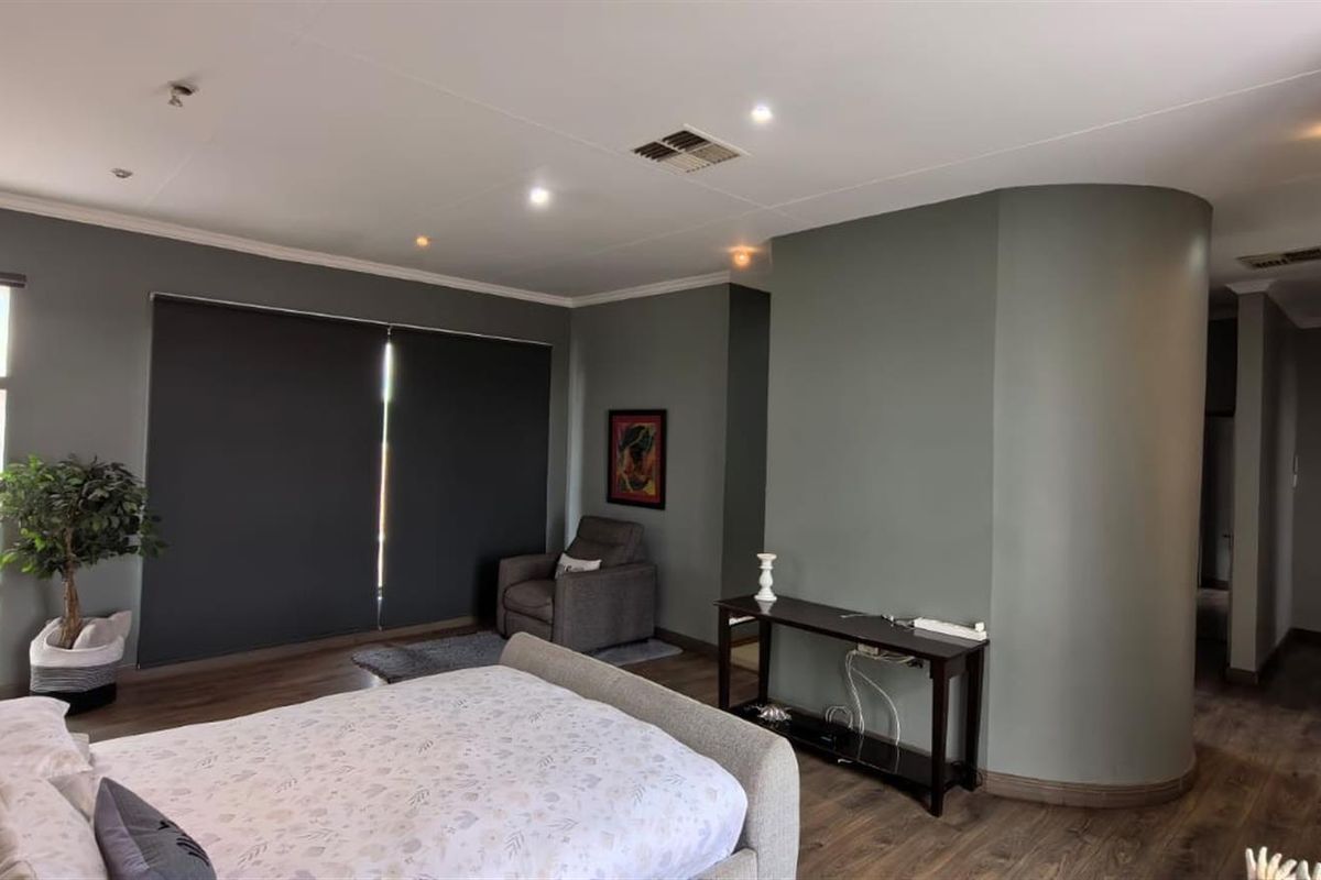 Spacious bedroom featuring modern laminate flooring, recessed downlighting, a unique curved feature wall, and ample built-in cupboard storage.