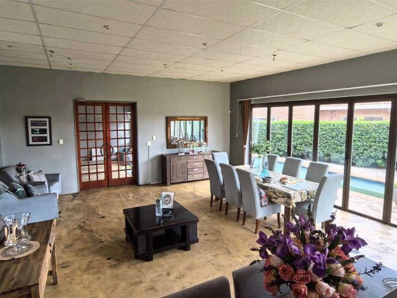 Spacious open-plan living and dining area featuring polished concrete floors, a suspended ceiling, and large sliding glass doors providing access to the pool area.