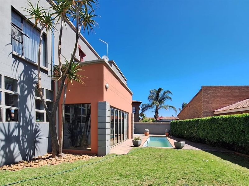 Rear exterior view featuring a private swimming pool, paved patio area, and well-maintained garden with established hedge boundaries.