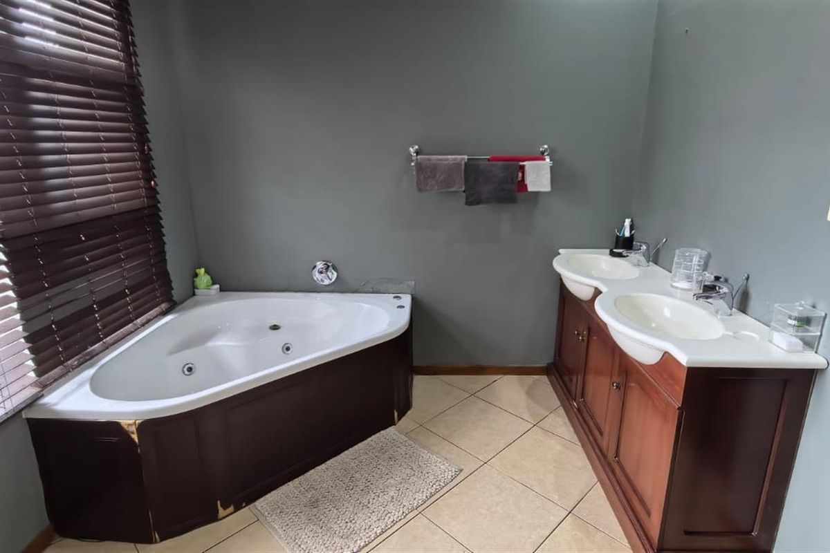 Bathroom featuring a corner spa bath, double vanity with wooden cabinetry, and tiled flooring, offering a functional layout with potential for cosmetic updates.