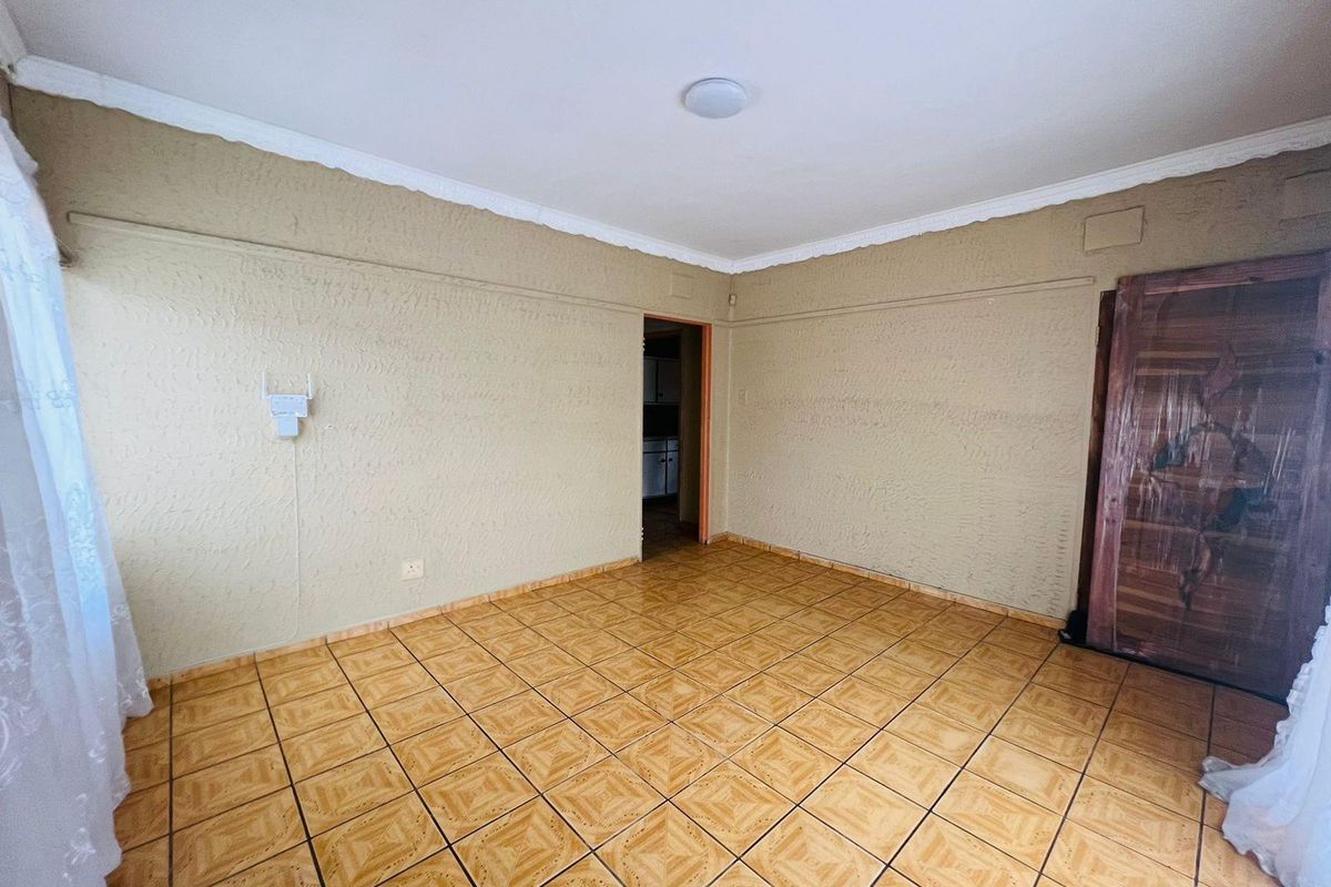 An empty living room featuring textured walls, ceramic tiled flooring, and decorative ceiling cornicing, offering a blank canvas for renovation.