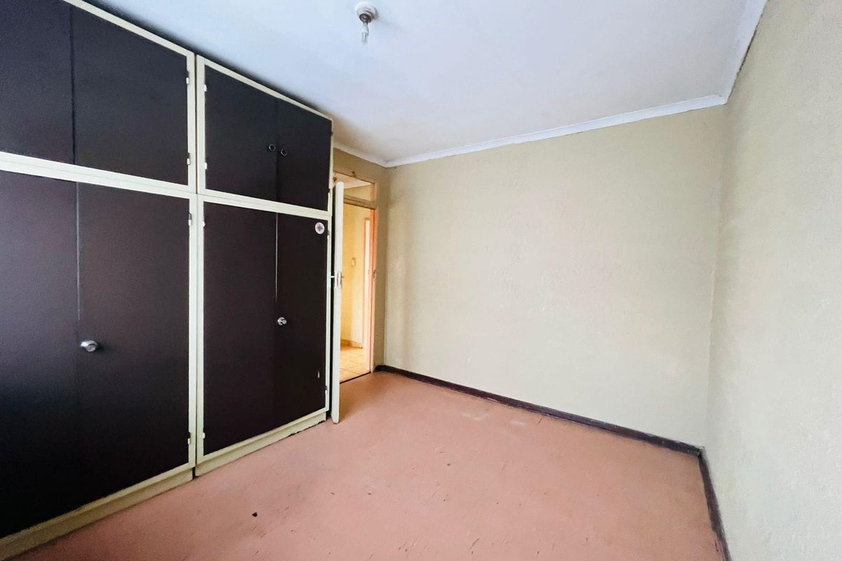 A vacant bedroom featuring built-in cupboards, neutral wall finishes, and worn flooring, offering a blank canvas for renovation or interior design updates.