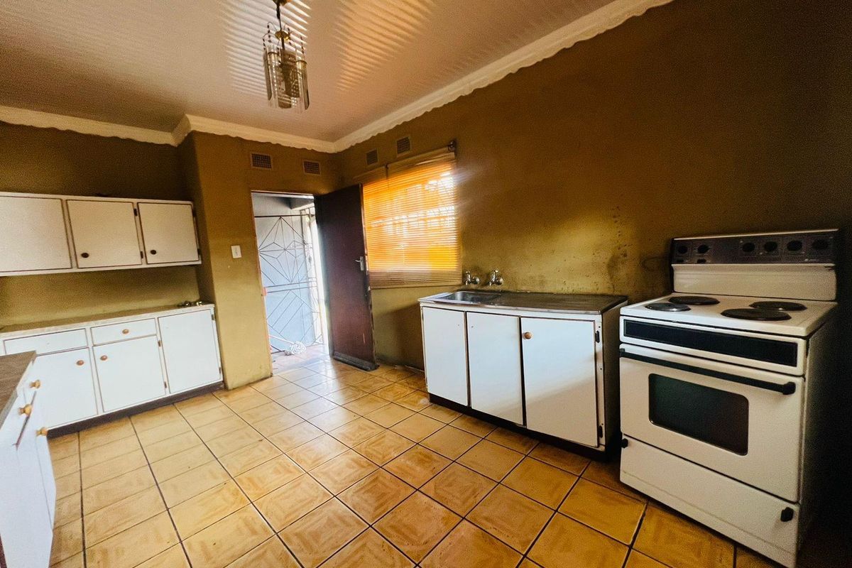 A functional kitchen featuring tiled flooring, built-in cabinetry, and a freestanding electric stove, with direct access to an exterior security gate.