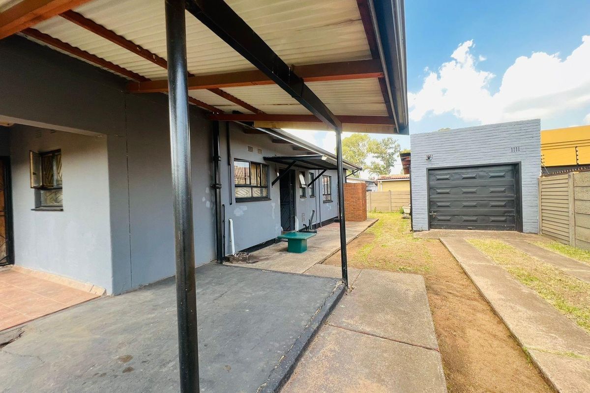 Rear exterior view featuring a covered patio area, concrete pathway, and a detached garage with a paved driveway.