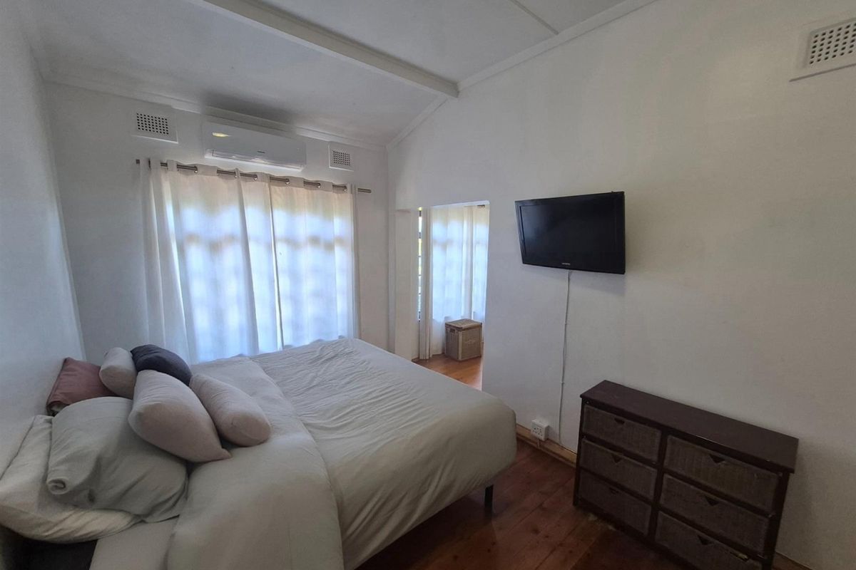 A bedroom featuring timber flooring, a wall-mounted air conditioning unit, and a vaulted ceiling with integrated ventilation grilles.