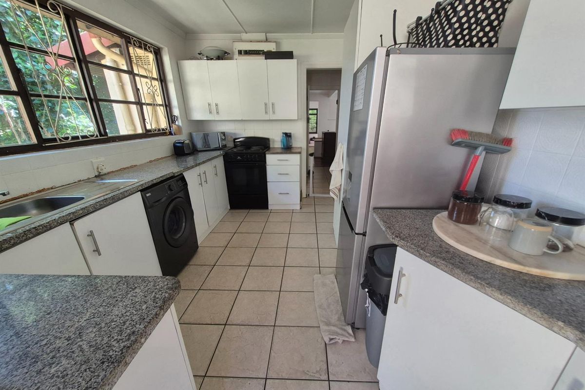 Functional kitchen featuring white cabinetry, granite-look countertops, tiled flooring, and integrated space for laundry appliances.