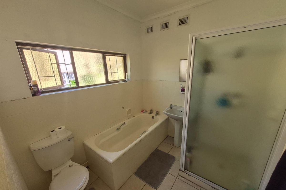 A functional bathroom featuring a built-in bathtub, pedestal basin, and a separate shower enclosure with frosted glass doors.
