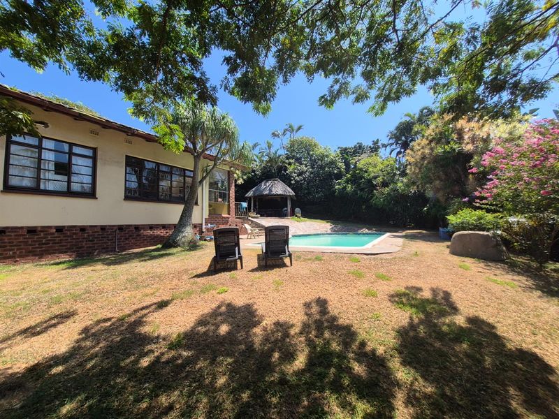 A spacious rear garden featuring a swimming pool, a thatched gazebo, and mature trees, providing a private outdoor entertainment area.