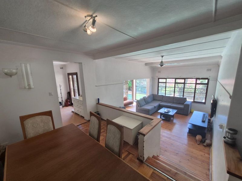 Open-plan living and dining area featuring polished timber flooring, split-level layout, and large windows providing natural light and garden views.