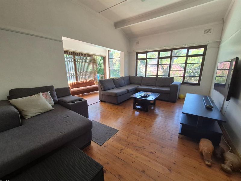 Spacious open-plan living area featuring high vaulted ceilings, polished timber flooring, and large windows providing ample natural light and garden views.