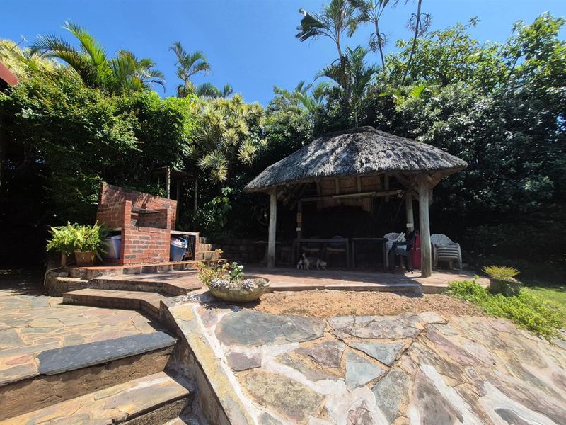 Outdoor entertainment area featuring a built-in brick braai and a thatched lapa set within a landscaped garden.