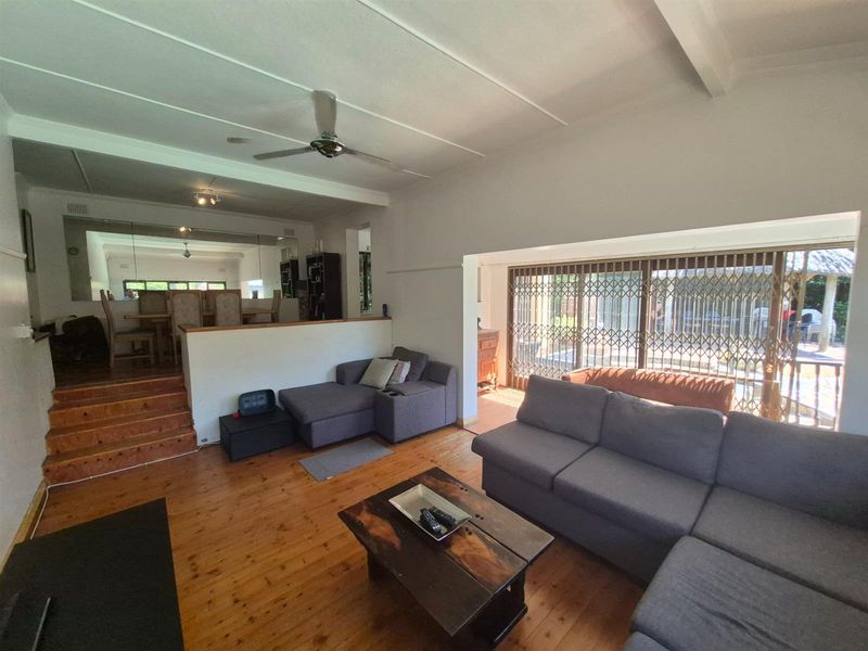 Spacious open-plan living area featuring timber flooring, a split-level layout, ceiling fan, and large sliding doors leading to an outdoor patio.