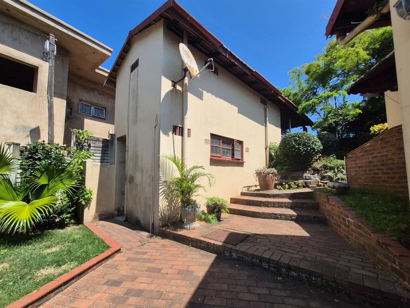 A view of the rear exterior of the property featuring brick paved pathways, tiered garden steps, and established landscaping.