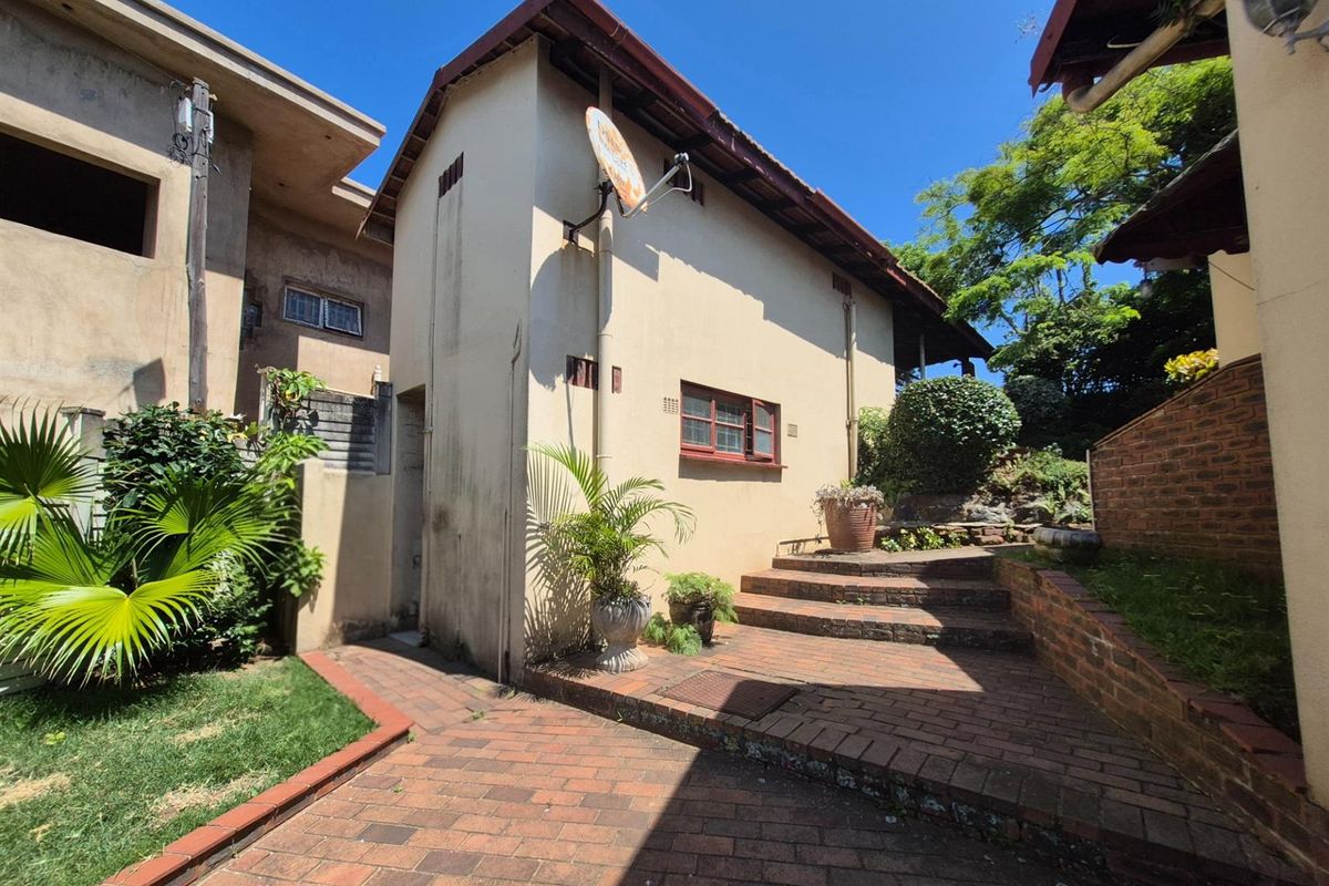 A view of the rear exterior of the property featuring brick paved pathways, tiered garden steps, and established landscaping.