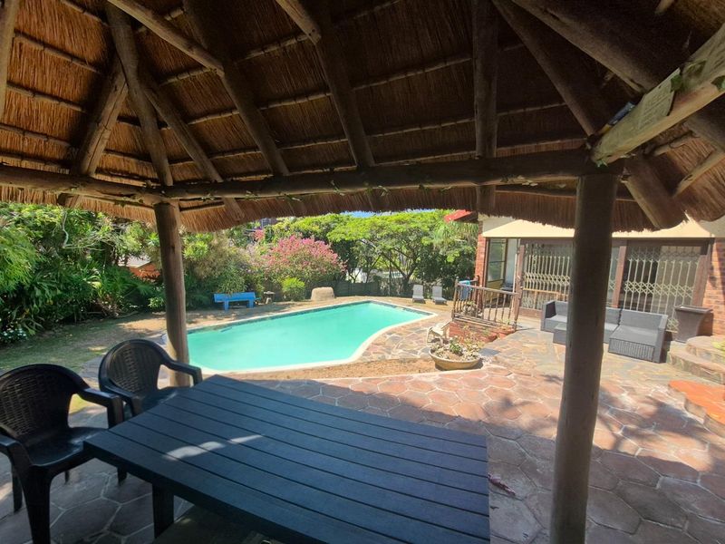 Outdoor entertainment area featuring a thatched lapa overlooking a swimming pool and landscaped garden.