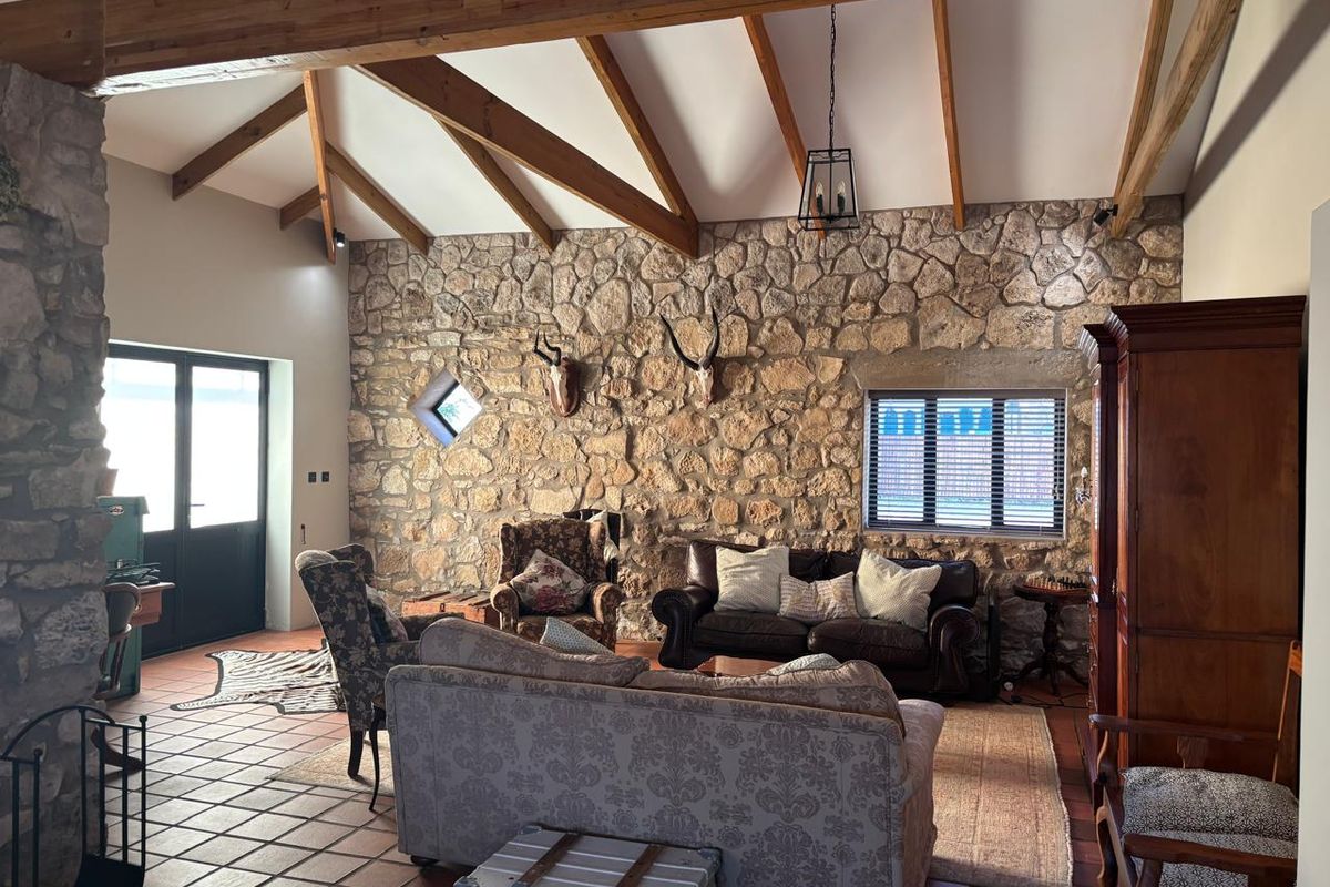 Spacious living room featuring a vaulted ceiling with exposed timber beams and a prominent natural stone feature wall.