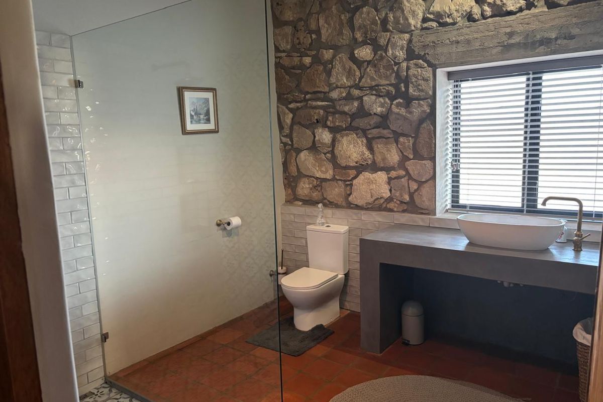 A rustic bathroom featuring exposed stone walls, a concrete vanity with a vessel sink, and a glass-enclosed shower with subway tile accents.