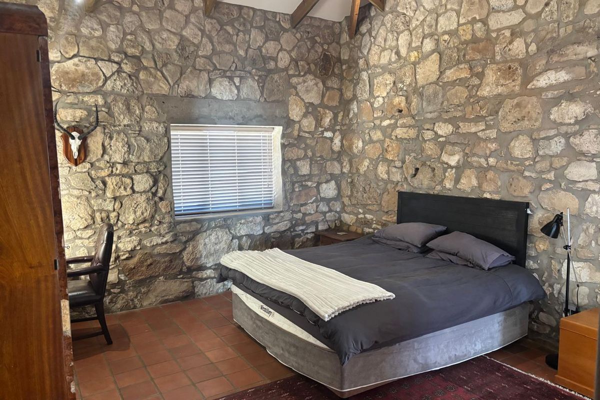 Rustic bedroom featuring exposed natural stone walls, vaulted timber beam ceiling, and terracotta floor tiles, creating a warm and character-filled living space.