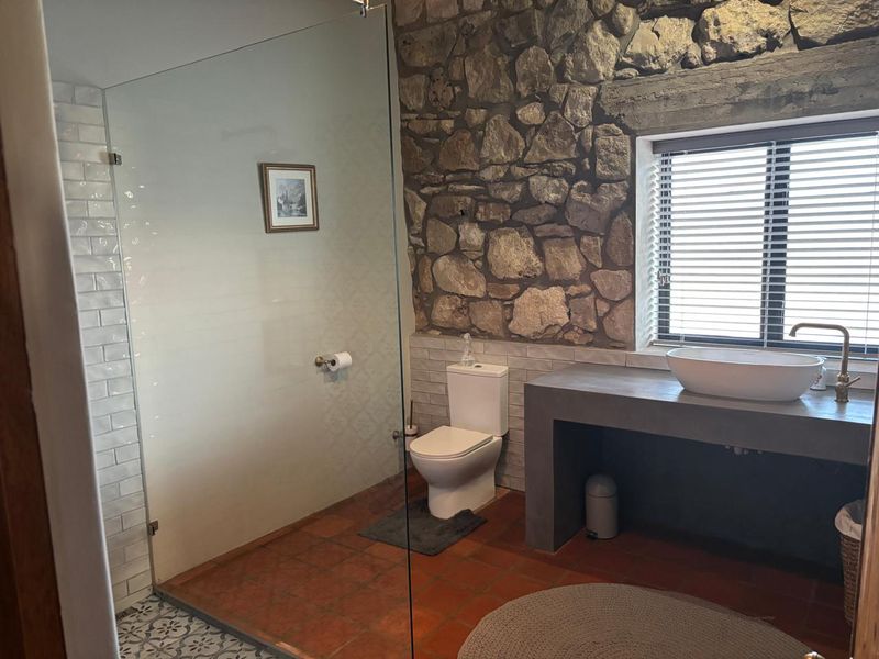 A rustic bathroom featuring exposed stone walls, a concrete vanity with a vessel sink, and a glass-enclosed shower with subway tile accents.