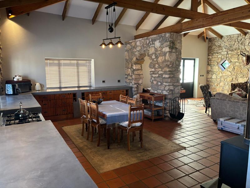 Spacious open-plan kitchen and living area featuring exposed timber roof trusses, natural stone feature walls, and durable terracotta floor tiling.